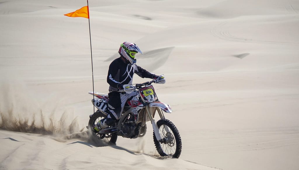 Motocross rider in black gear navigating white desert dunes