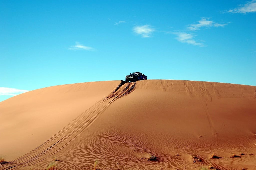 4x4 vehicle atop a steep desert dune under clear blue sky