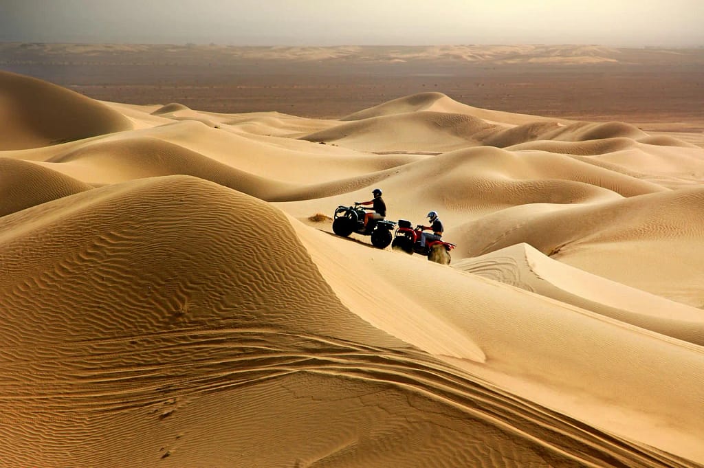  Two ATVs climbing sandy dunes in a desert landscape.