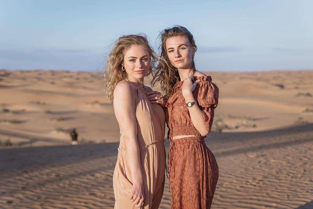 Two women standing in the Dubai desert wearing light, breathable dresses in neutral tones, demonstrating stylish and practical outfits for what to wear in Dubai desert safa