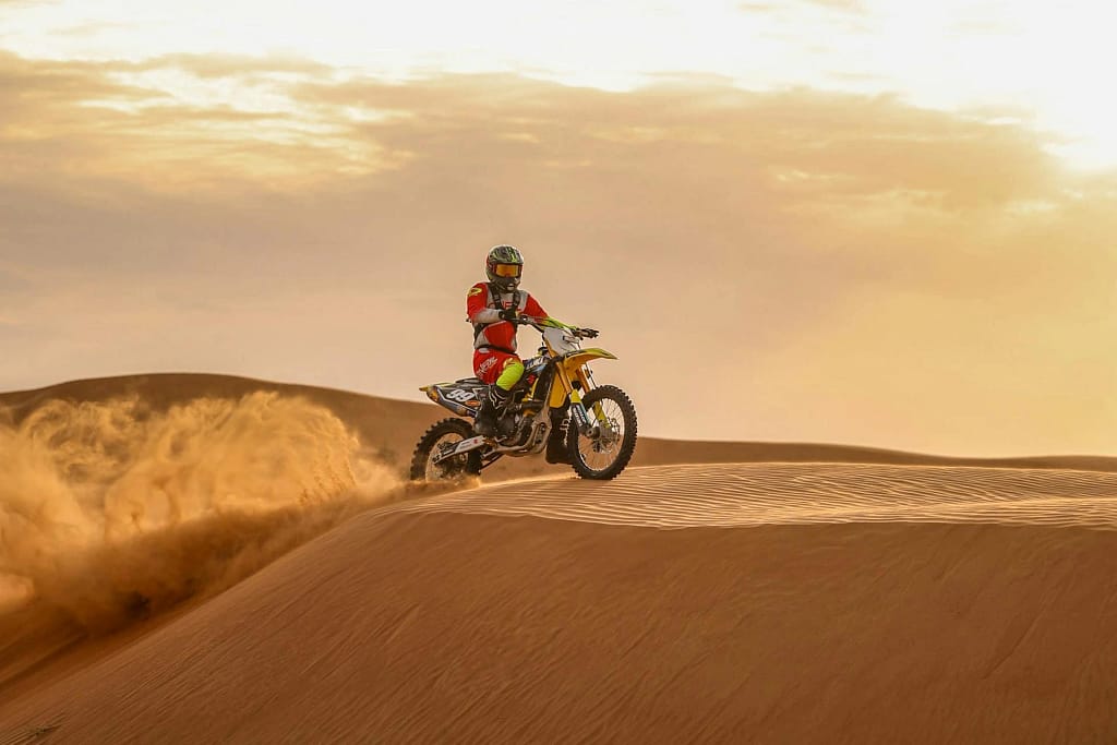 Dirt biker riding over sand dunes at sunset in Dubai