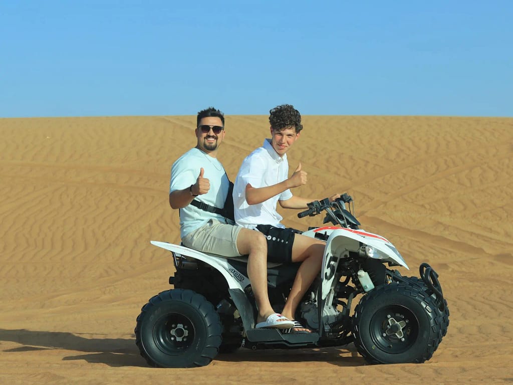  Two people enjoying a ride on an ATV in the desert, giving thumbs up.